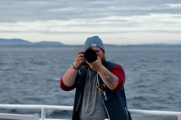 A Orca Spirit staff photographer snapping a picture onboard a covered vessel. 