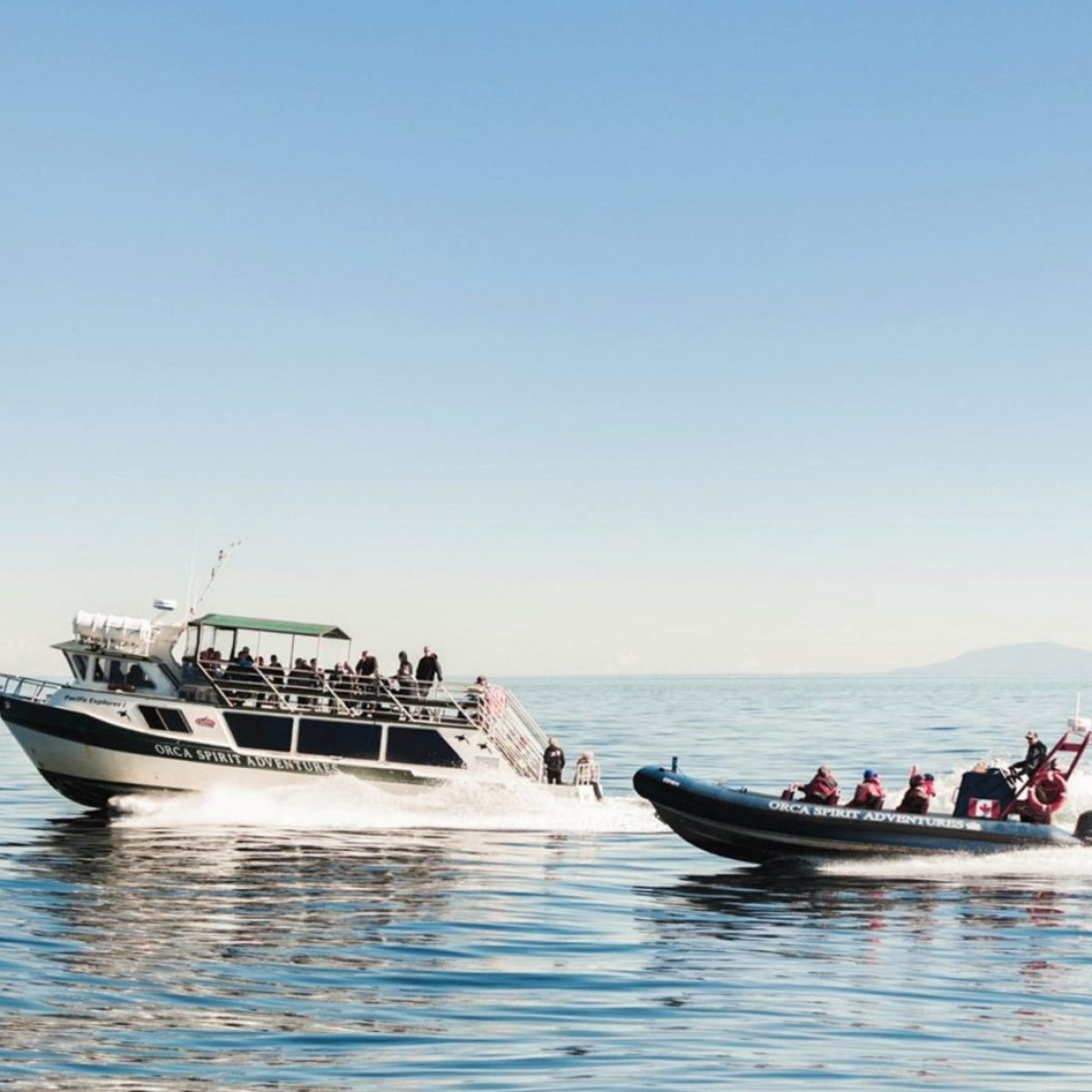 Two boats on calm sea, one larger and one smaller, both with passengers, clear sky.