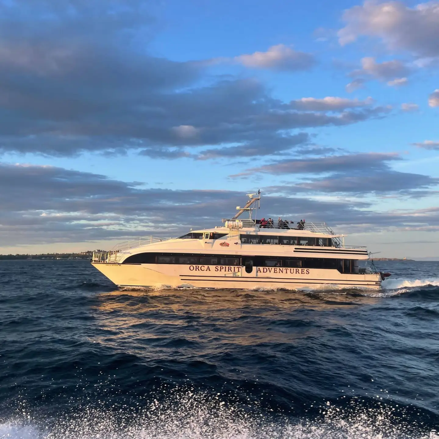 A boat named Orca Spirit Adventures on the ocean under a blue sky with clouds.