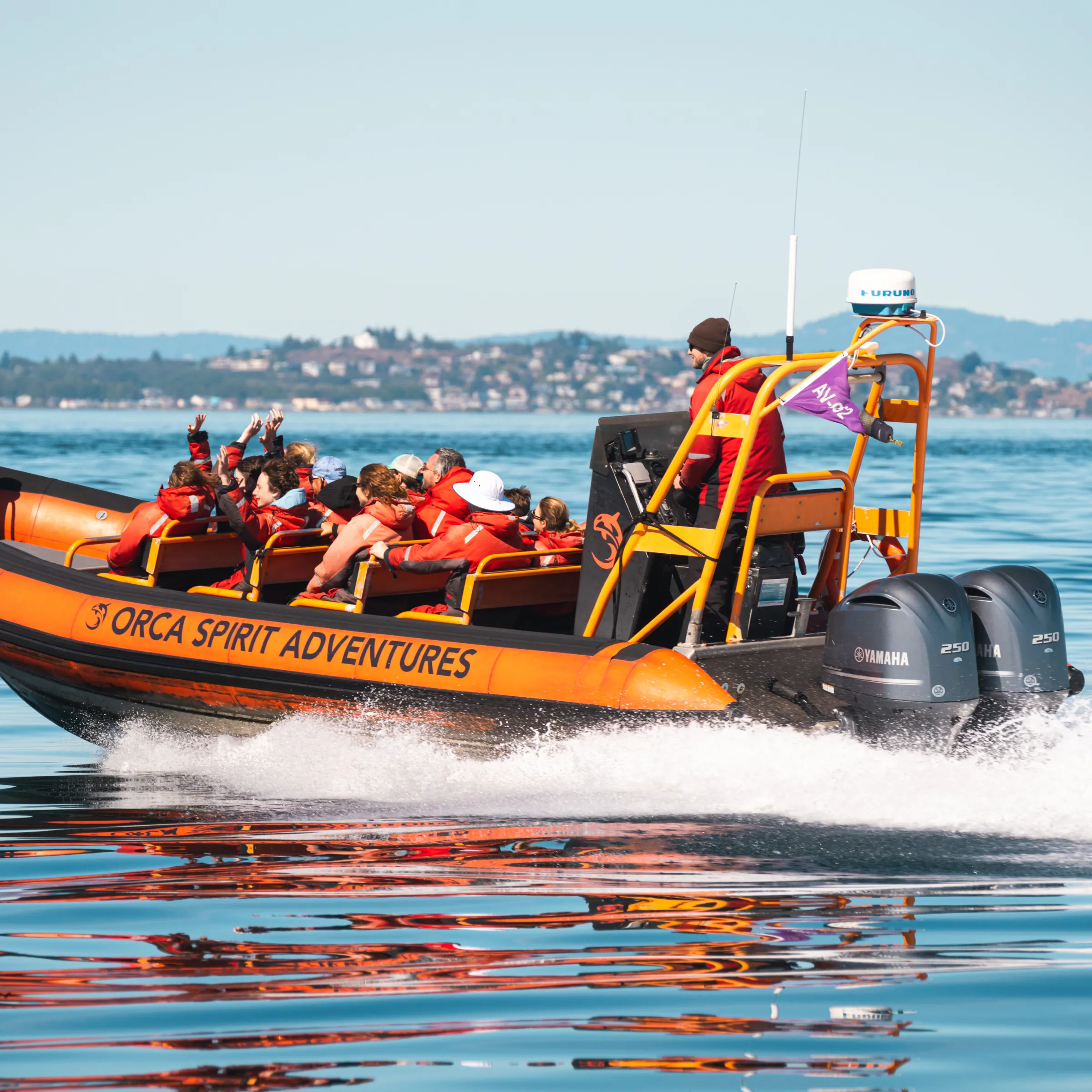 Orange boat with people in life jackets on a calm sea near a distant coastline.