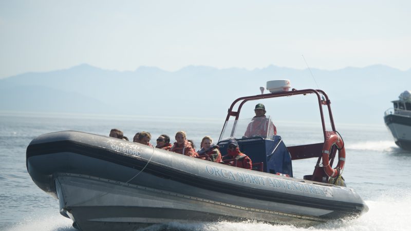 Two boats on the water with people in life vests; mountains in the background.