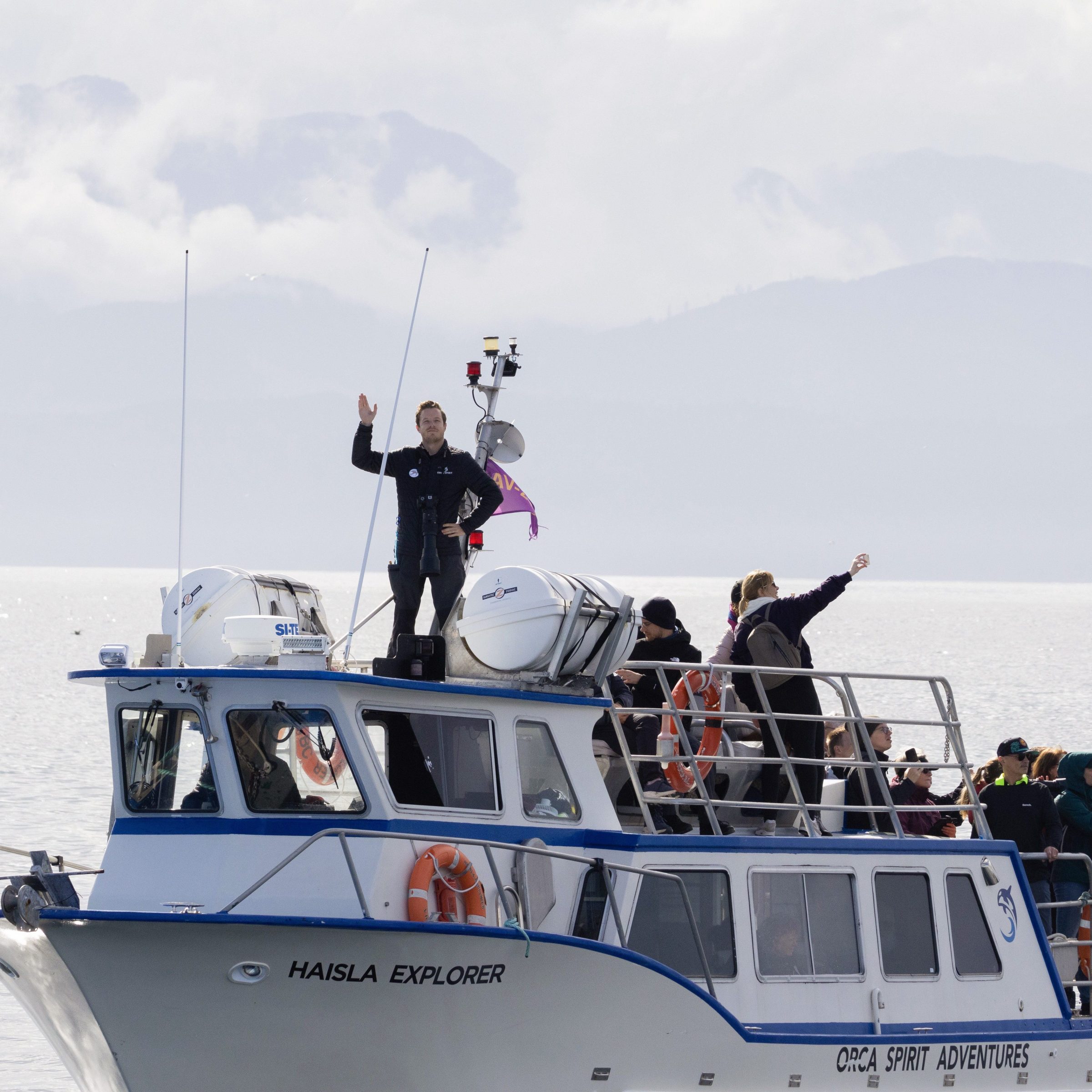 People on a boat named 'Haisla Explorer' with mountains in the background.