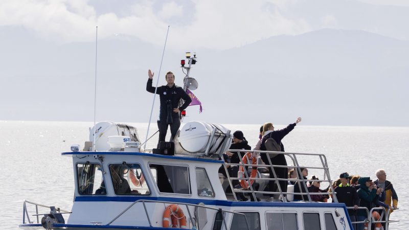 People on a boat named 'Haisla Explorer' with mountains in the background.