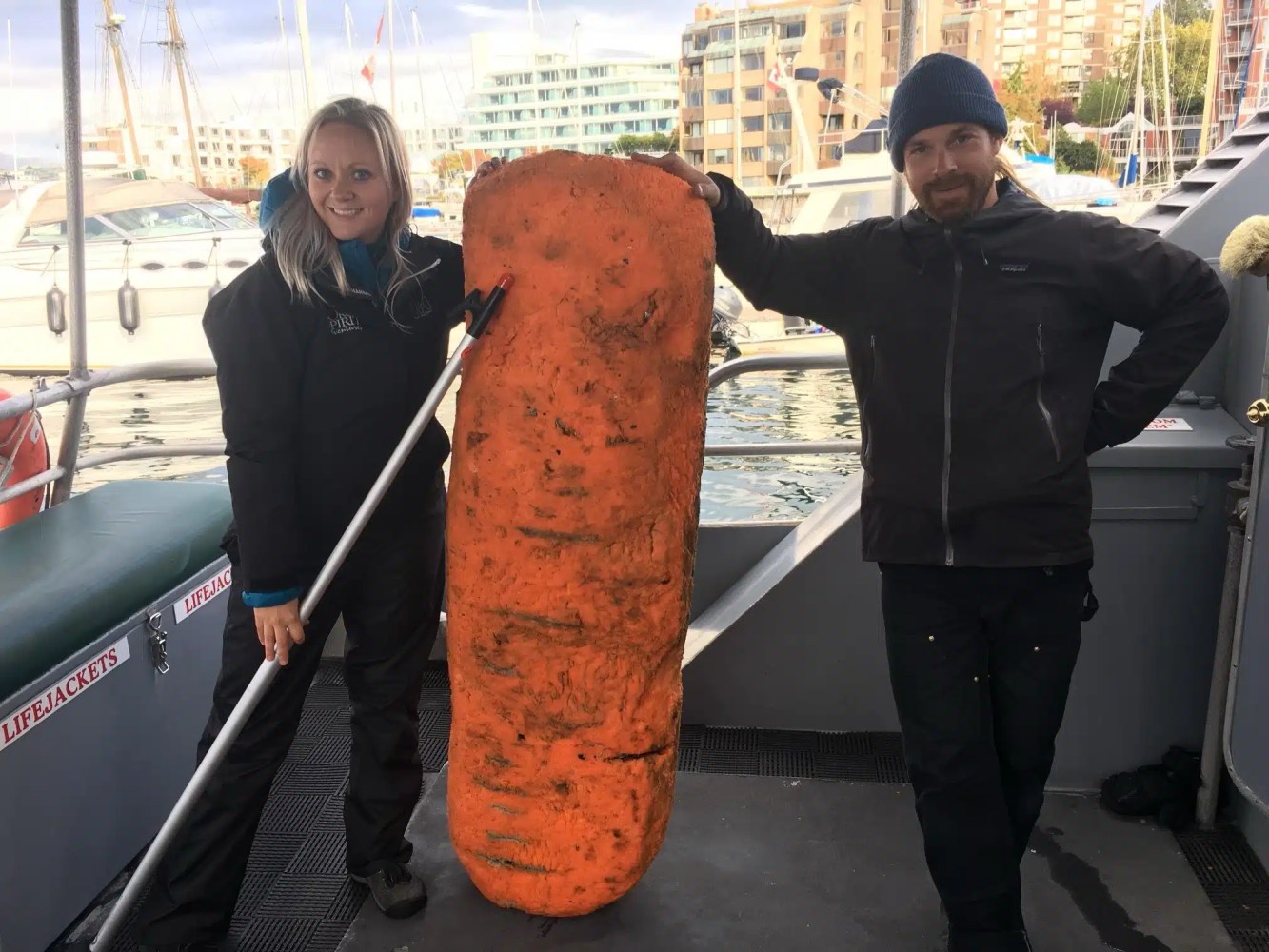 Two people on a boat with a giant carrot-shaped object between them.