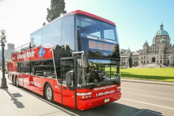 Red double-decker tour bus in front of a historic building on a sunny day.