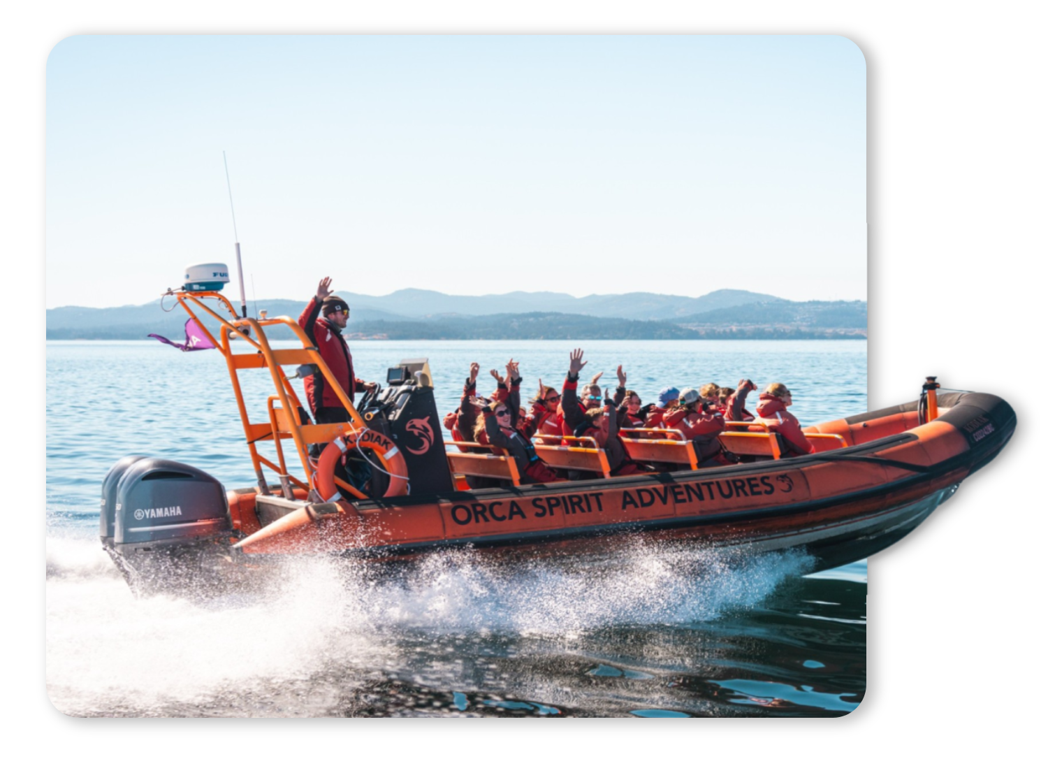 People on an orange boat with 'Orca Spirit Adventures' logo, waving on the sea.