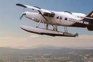 Seaplane with 'Harbour Air' branding flying over a city landscape.